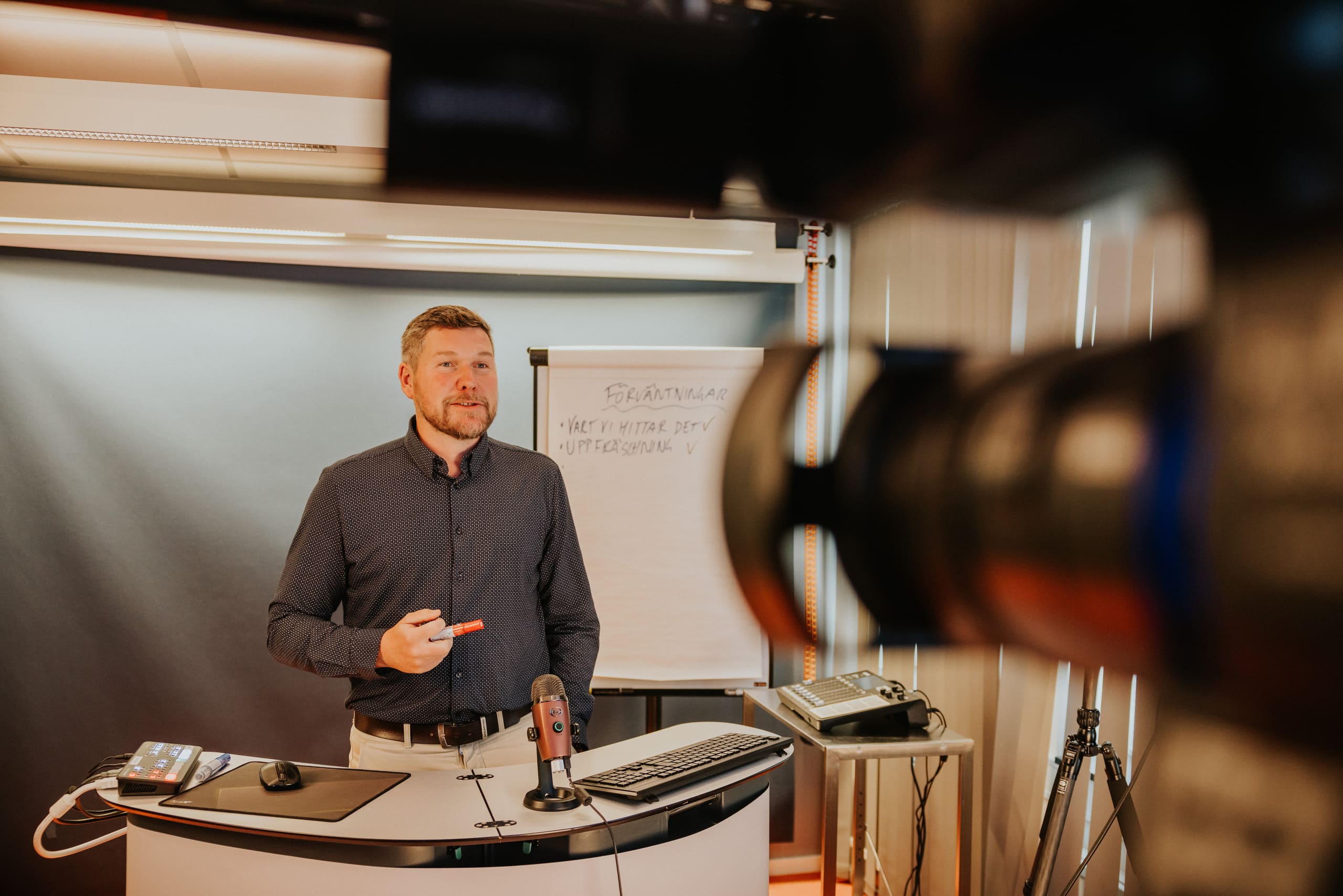 En man håller en presentation framför ett blädderblock under en utbildning eller workshop, med en videokamera i förgrunden.