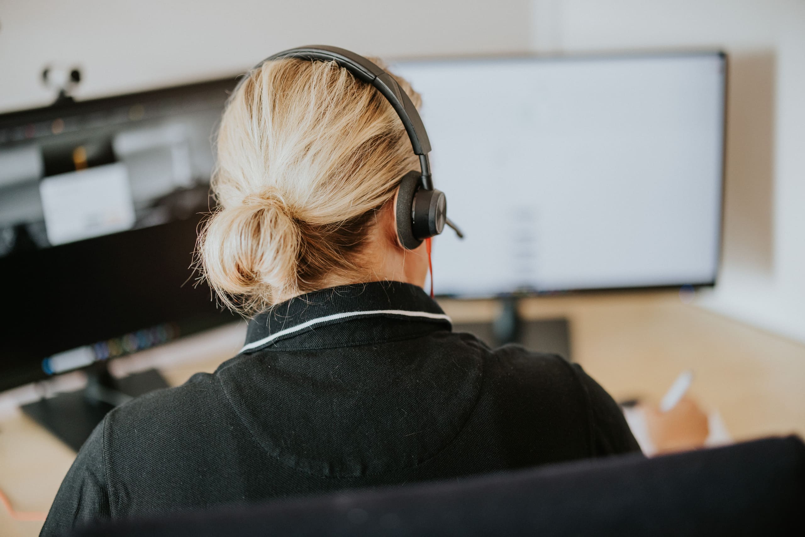En person med headset sitter framför två datorskärmar och arbetar vid ett skrivbord.